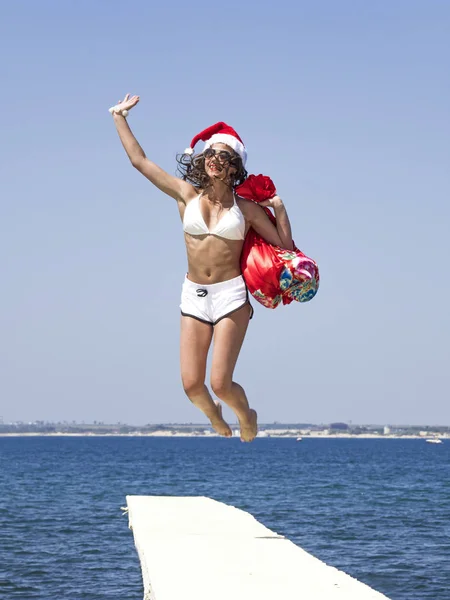 ビーチでジャンプ サンタの帽子を着て幸せな少女 — ストック写真