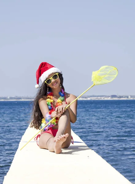 クリスマスのお祝いの時にネットで桟橋に座っているサンタさんの帽子の女性 — ストック写真
