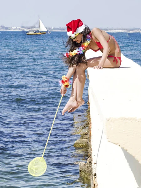 桟橋の上に座って、クリスマスのお祝いの時にネットで釣りのサンタさんの帽子の女性 — ストック写真