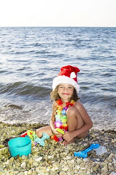 Kleiner Junge mit Weihnachtsmütze und Spielzeug am Strand — Stockfoto