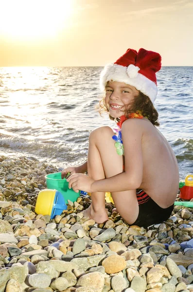 Маленький мальчик в шляпе Санты с игрушками на пляже — стоковое фото