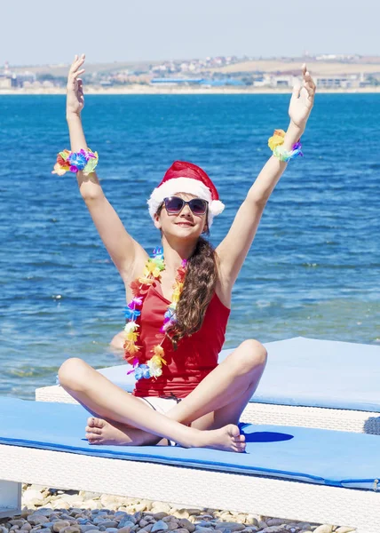 Portrait de Noël jolie jeune femme souriante en chapeau de Père Noël rouge sur la plage sur fond de mer — Photo