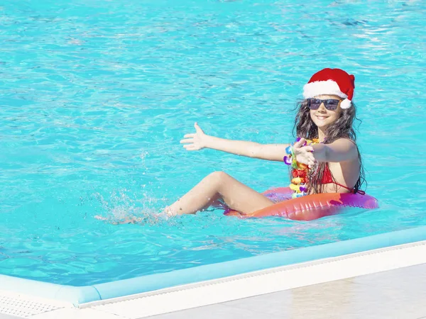 Yüzme havuzunda şişme çörek ile Noel Baba'nın şapkalı güzel bir genç kadın — Stok fotoğraf
