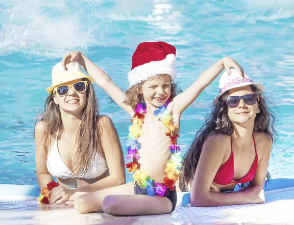 Chicas felices y bebé sentado cerca de la piscina durante la Navidad — Foto de Stock