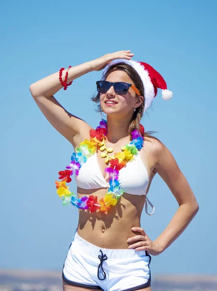Різдвяний портрет досить молодої усміхненої жінки в червоному капелюсі Санта на пляжі над морським тлом — стокове фото