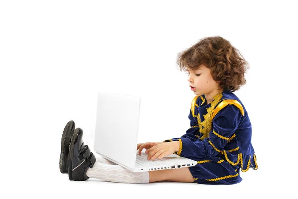Fiú, ő fehér laptop számítógéppel böngészés az interneten. Személyi számítógép és egy fiú öltözött, mint egy király — Stock Fotó