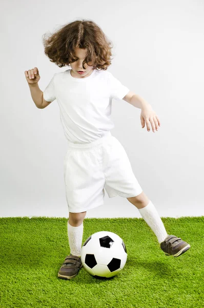 Молодой футболист играет в футбол на траве. Серый фон . — стоковое фото