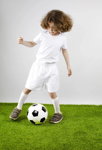 Молодой футболист играет в футбол на траве. Серый фон . — стоковое фото