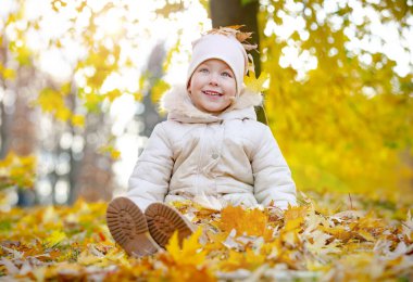 Mutlu kız sonbahar parkında eğleniyor. Küçük kız karışık ve sonbahar yaprakları serpiştirilmiş..