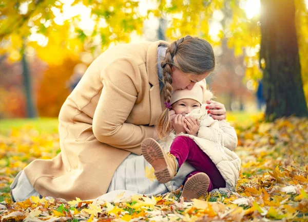 mother daughter love hug at autumn city park fall season. Family in the autumn park among yellow leaves. Young mother with a little daughter play with leaves in the autumn park. Autumn mood