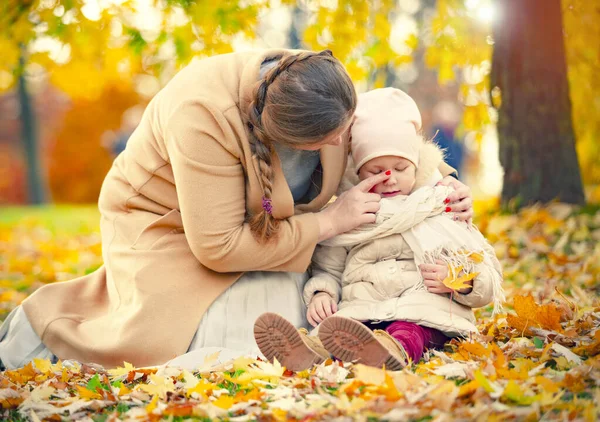 mother daughter love hug at autumn city park fall season. Family in the autumn park among yellow leaves. Young mother with a little daughter play with leaves in the autumn park. Autumn mood