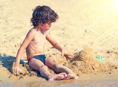 Tropik sahilde oynayan çocuklar. Çocuklar yaz aile tatilinde denizde oynarlar. Kum ve su oyuncakları, küçük çocuklar için güneş koruması. Küçük çocuk kum kazıyor, okyanus kıyısında kale inşa ediyor..