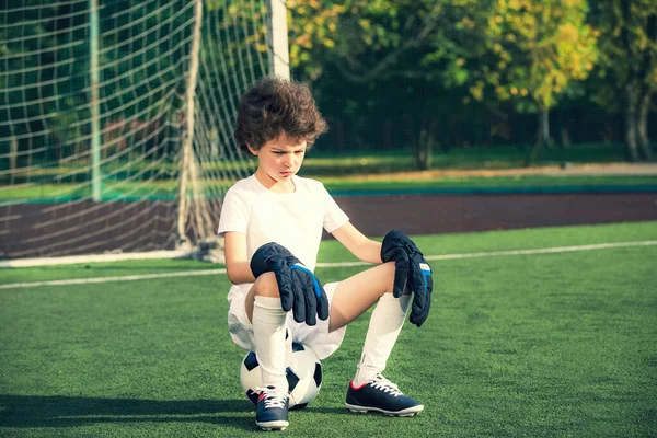 Zomer voetbaltoernooi.emoties en vreugde van het spel. Jonge doelpunten zittend op een bal. Jongensdoelman in voetbal sportkleding op het stadion met bal. Sportconcept. — Stockfoto