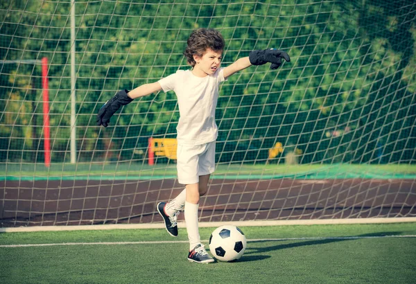 Nyári focibajnokság fiatal gyerekeknek. futball klub. érzelmek és öröm a játék. Fiatal kapus. Gyerekek - foci bajnok. Fiú kapus a futball sportruházatban a stadionban labdával. Sportkoncepció. — Stock Fotó