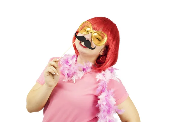 Portrait of a young chubby girl in a red wig with a carnival mustache on her face