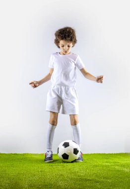 Genç futbolcu gri zeminde topu tekmeliyor.