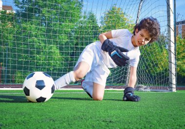 Genç erkek ya da çocuk spor yapmak ve spor yapmak için futbol oynuyor. Kaleci çocuk topa ayağıyla vurmaya çalışıyor.