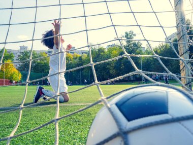 Heyecanlı futbolcu çocuk gol üstüne gol attı. Genç çocuk ya da çocuk spor yapmak için futbol ya da spor yapıyor. Gol ağlarının arkasından bak. seçici odak