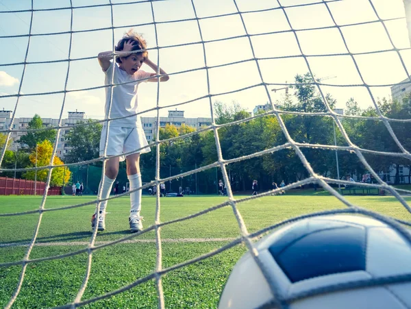 Young boy or kid plays soccer or football sports for exercise and activity. View from behind the goal nets. selective focus