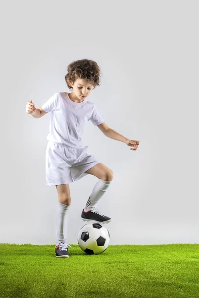 Junior soccer player kicking a ball isolated on gray background
