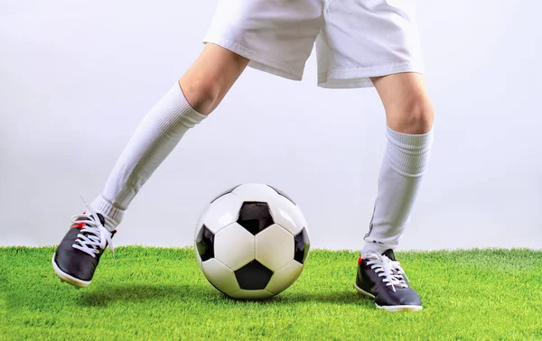Football training for children. Soccer training dribbling. Indoor soccer young player with soccer ball in artificial grass studio. Player in white uniform. Grey background.