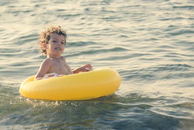 Mutlu Çocuk, Karadeniz 'de yüzen sarı şişme bir daire üzerinde. Boşluğu kopyala