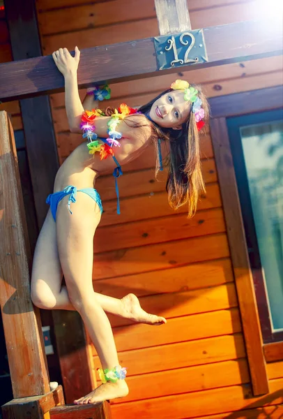 하와이 액세서리를 소녀와 파란색 수영복을 해변의 방갈로의 가장자리에서 — 스톡 사진