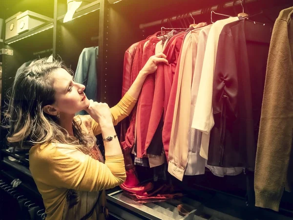 Woman chooses clothes at fashionable shop. side view of mature woman choosing clothes in clothing store