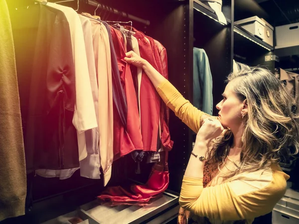 Woman chooses clothes at fashionable shop. side view of mature woman choosing clothes in clothing store