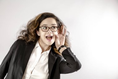 Genç ve güzel bir kadın neşeli ve meraklı görünüyor, dinliyor, gizli bir konuşma ya da dedikodu duymaya çalışıyor. Açığa çıkma ve merak konsepti. Gri üzerine izole edilmiş. Boşluğu kopyala