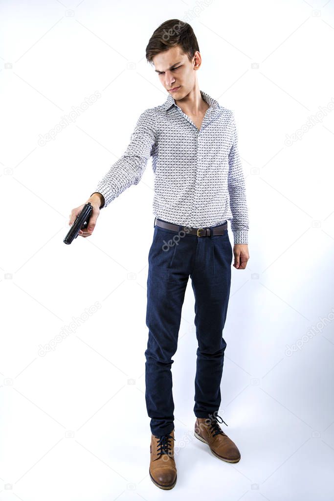 Profile view of a young man wearing a business attire holding a gun aiming down. Isolated on white, copy space