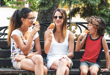Dışarıda birlikte dondurma yiyen dört mutlu çocuktan oluşan bir grup. Parktaki ahşap bankta oturmuş dondurma yiyen üç sevimli çocuk. eğlenceli tatil konsepti