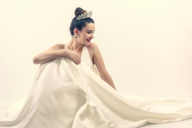 Lüks bir gelinlik içinde çok genç ve güzel bir gelin ve taç gülümsüyor ve sağdaki boş alana bakıyor. Boşluğu kopyala