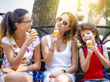 Dışarıda birlikte dondurma yiyen dört mutlu çocuktan oluşan bir grup. Parktaki ahşap bankta oturmuş dondurma yiyen üç sevimli çocuk. eğlenceli tatil konsepti