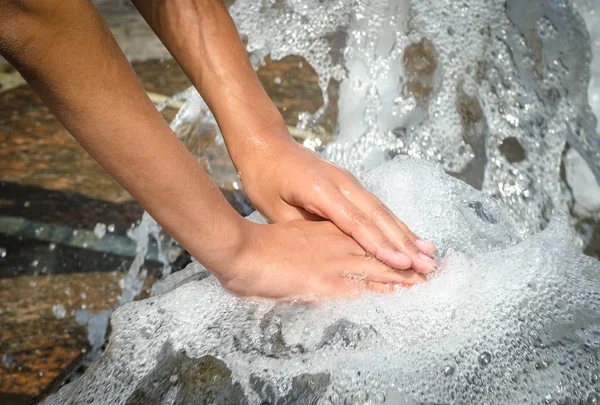 Hands touch the fountain. A stream of water from the fountain is touched by hands. Freshness and coolness concept