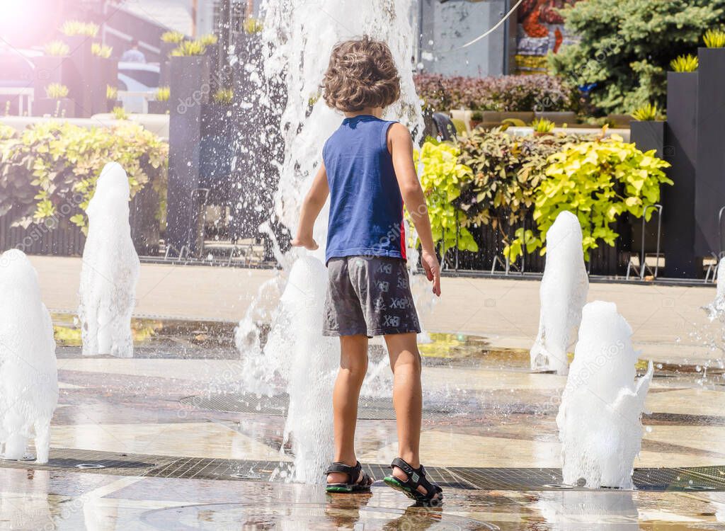 Child playing with water at street fountain in summer. Little boy playing in a fountain