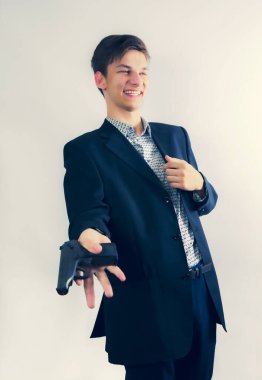 Gizli görevdeki genç gangster bir silah tutuyor ve koyu renk ceket giyiyor. Arka planda izole bir şekilde gülüyor. Seçici odak