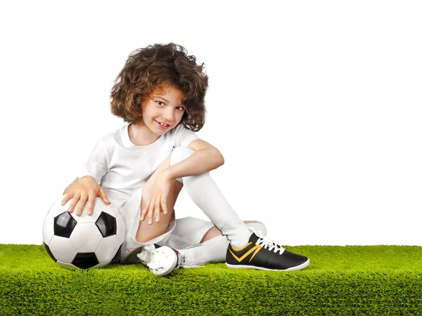 一个带着球的年轻足球运动员坐在体育场的草地上 — 图库照片