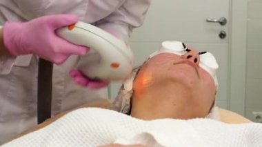 Profesyonel ekipmanlarla akne fototerapisi. Güzellik salonunda fotoğraf yenileme işlemi sırasında güzel bir kadın. Kozmetik kliniğinde lazer yüz bakımı. Donanım kozmetolojisi. 4K