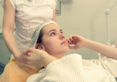 Güzellik kliniği kozmetoloji servisinde saç şapkası takan genç bir kadın. Doktor ameliyatı yapmaya hazırlanırken tıp yatağında dinleniyor.