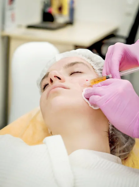 Cosmetologist does prp therapy on the face of a beautiful woman in a beauty salon. There is in vitro blood plasma, ready for injection. Cosmetology concept.