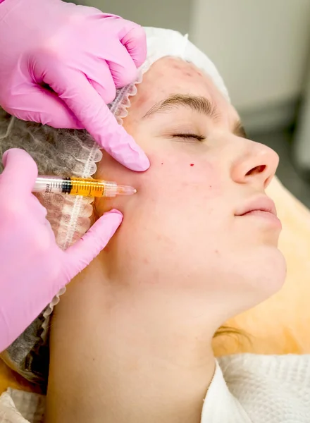 Kozmetik uzmanı güzellik salonunda güzel bir kadının yüzü üzerinde terapi uygular. Enjeksiyona hazır kan plazması var. Kozmetoloji konsepti. Profil
