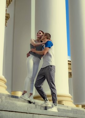 Yuna teenage couple hugging near the historical architectural columns in a city park on a hot day. Love concept