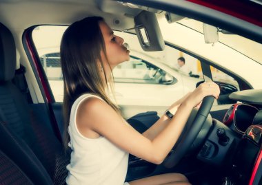 Galerideki yeni arabada oturan hoş bir kız. Yeni araba konsepti satın almak. Güzel genç bayan aynaya bakıyor.