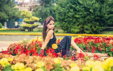 Çiçek dekorasyonundaki neşeli kız, güzel, enerjik kadınların teması. Şehir parkındaki çiçeklerin yanındaki kız. Kentsel peyzaj