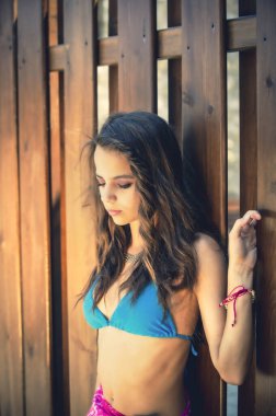 Tahta bir çite dayanmış mavi mayolu güzel bir kızın portresi..