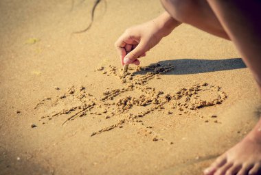 tic tac toe oyunu ya da XO oyunu kuma yazılır. Kumsalda oyun ve eğlence. Çocuk eli kuma bir kabuk çizer.