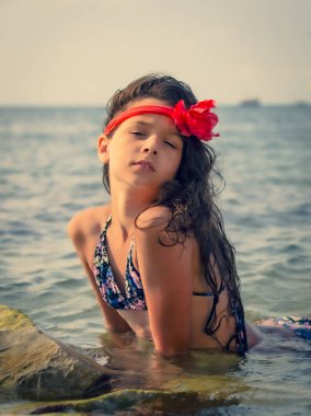 Kafasında kırmızı bir bandajla kayalık bir sahilde oturan gizemli hayalperest genç kız.