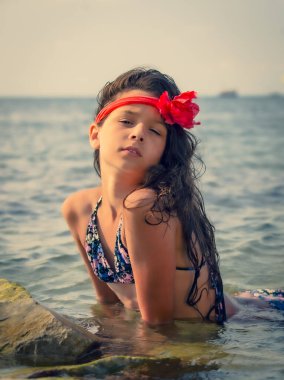 Kafasında kırmızı bir bandajla kayalık bir sahilde oturan gizemli hayalperest genç kız.