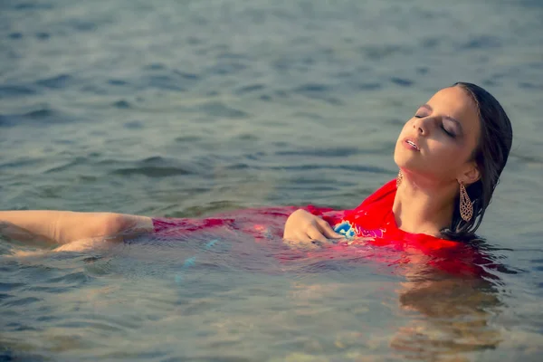 Nat Brunette Meisje Rode Jurk Zittend Het Water Het Strand — Stockfoto